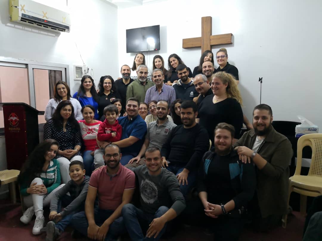 A community gathered for a group photo beneath a wooden cross