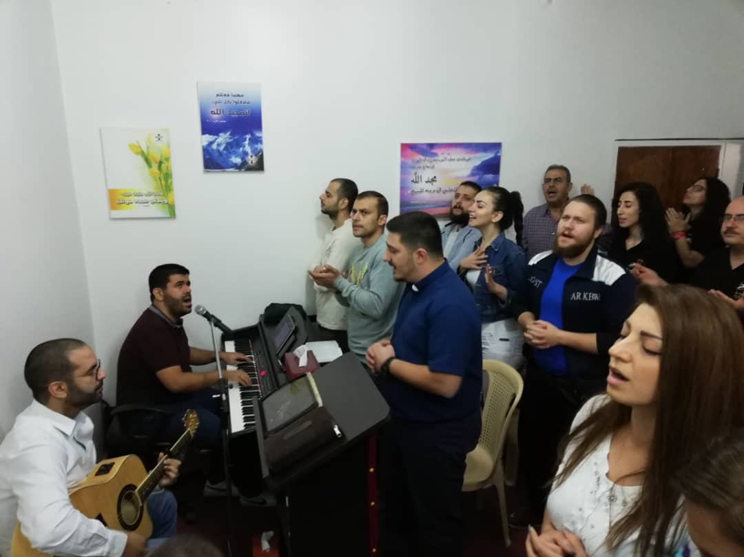 A gathering singing with piano and guitar accompaniment
